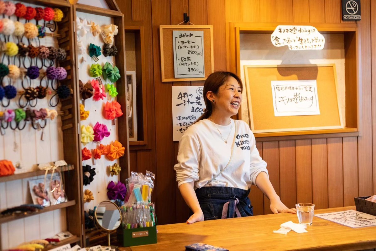 キノママ堂dining の店内で、リボンアクセサリーの棚を背に笑う MOEKO
